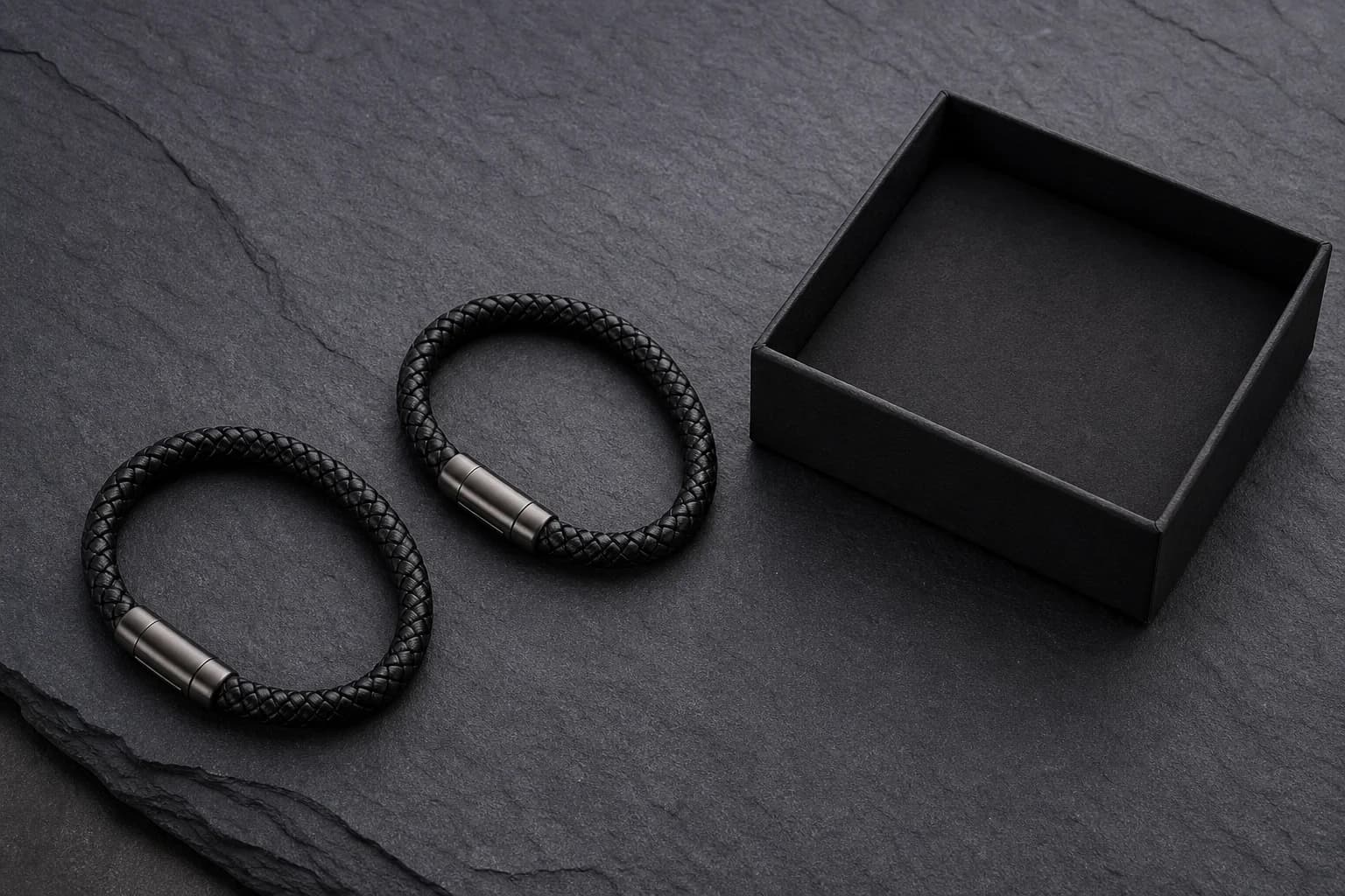 Two braided leather bracelets beside a matte black gift box